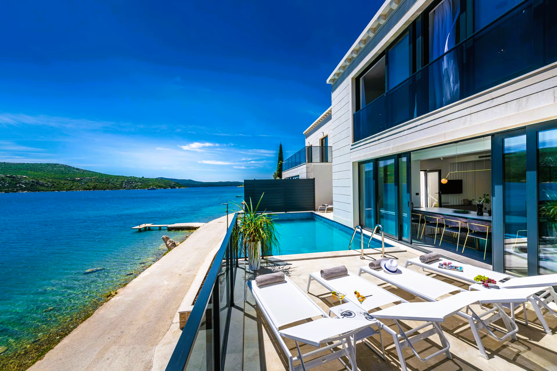 Luxury villa with pool overlooking a blue sea. White lounge chairs on the terrace.