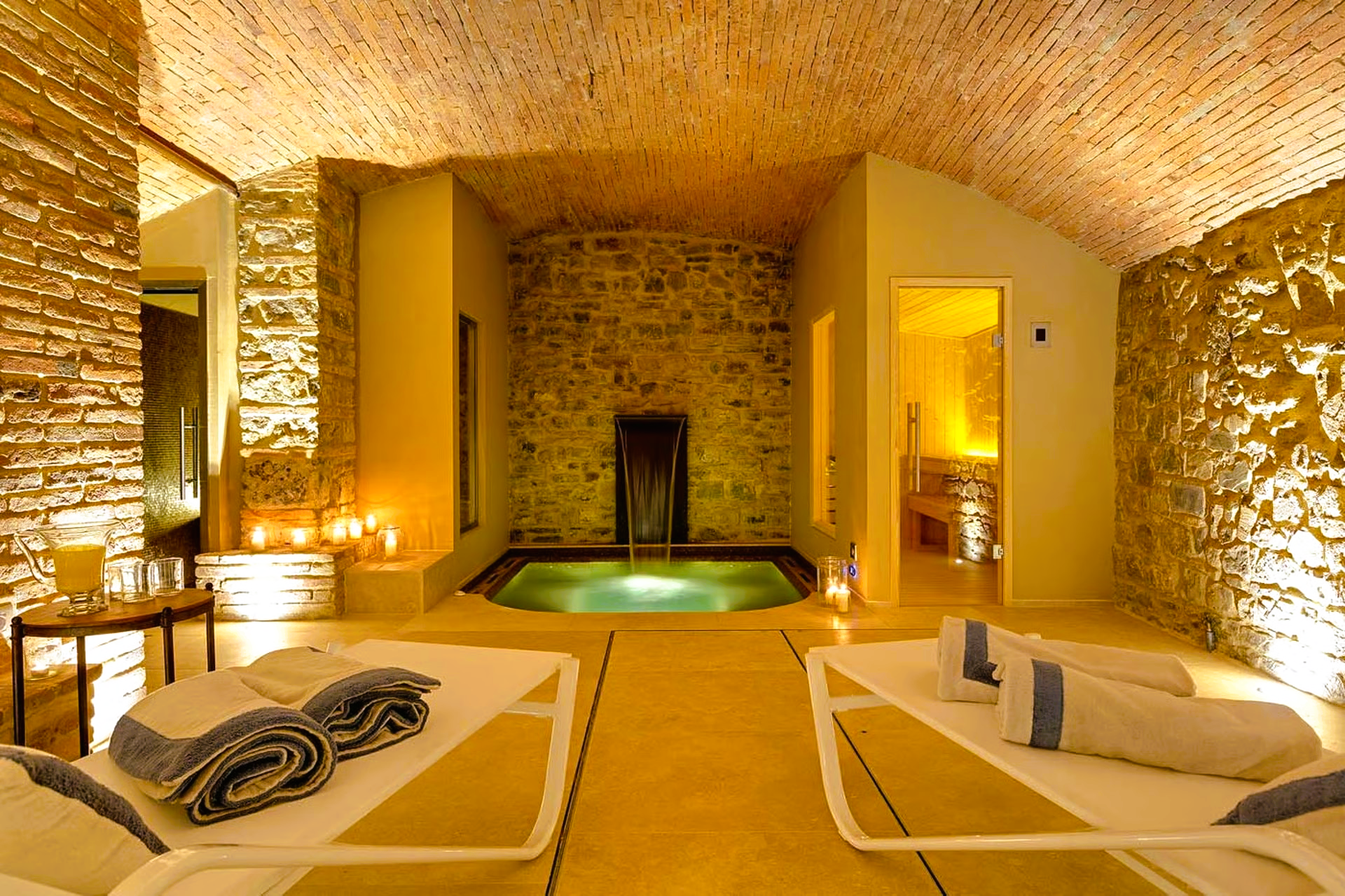 Spa interior with stone walls, a small pool, and two lounge chairs with towels.