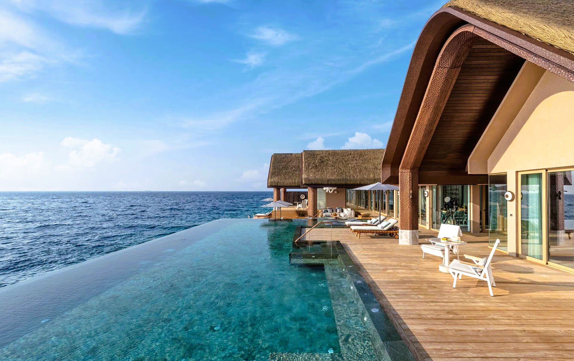Overwater villa with infinity pool overlooking the ocean; sunny, blue sky.