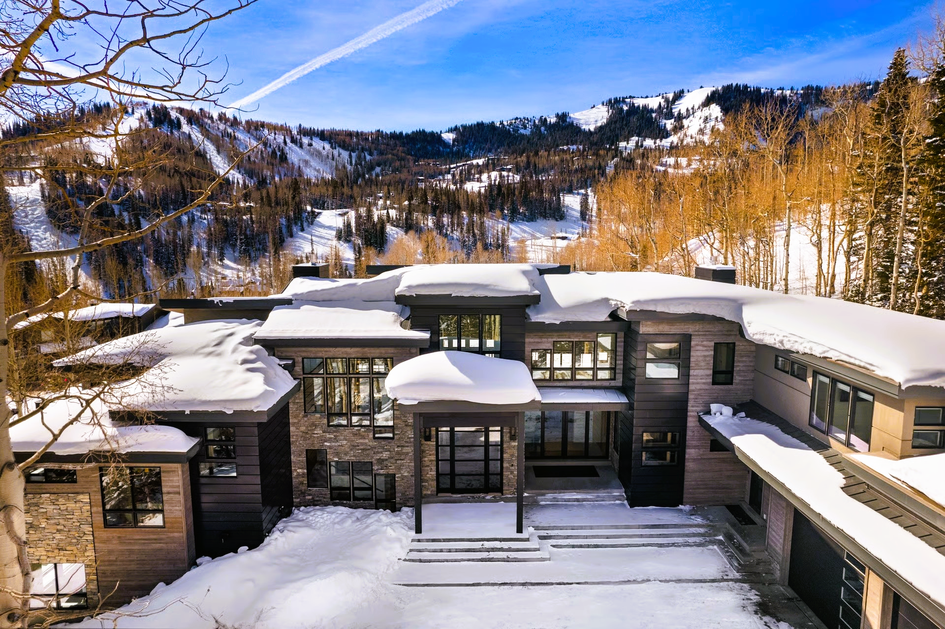 Modern, snow-covered luxury home with mountain backdrop.