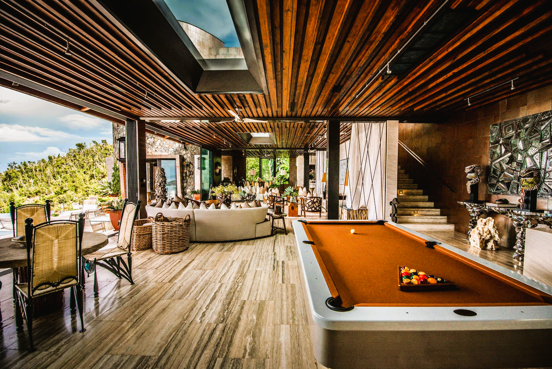 Indoor entertainment space with a pool table, sofa, and open view of trees and water.
