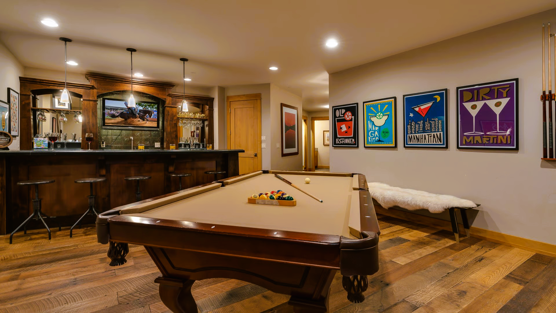 Game room with pool table, bar, and colorful cocktail posters. Wooden floors and bar.