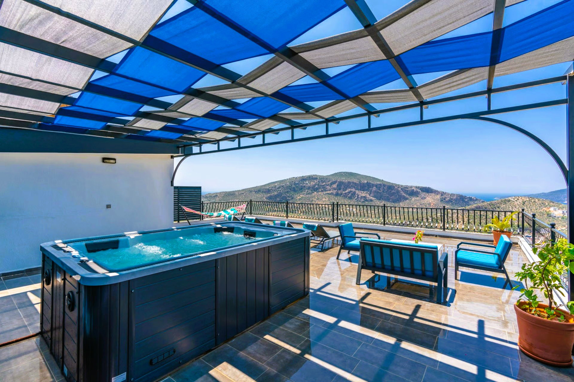 A rooftop patio with a hot tub, seating area, and mountain views under a blue and white canopy.