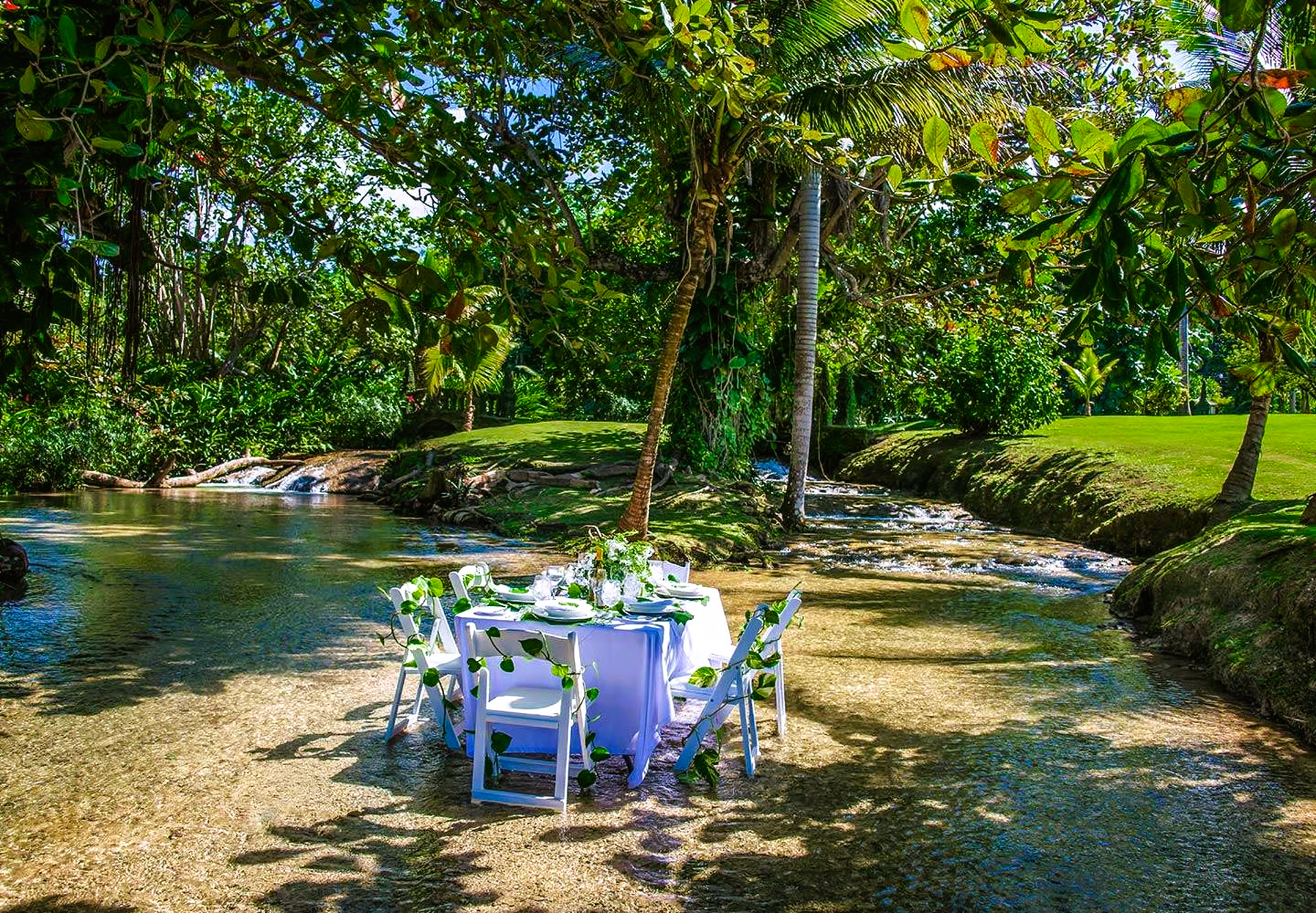 Wedding table set in shallow stream, surrounded by lush greenery.