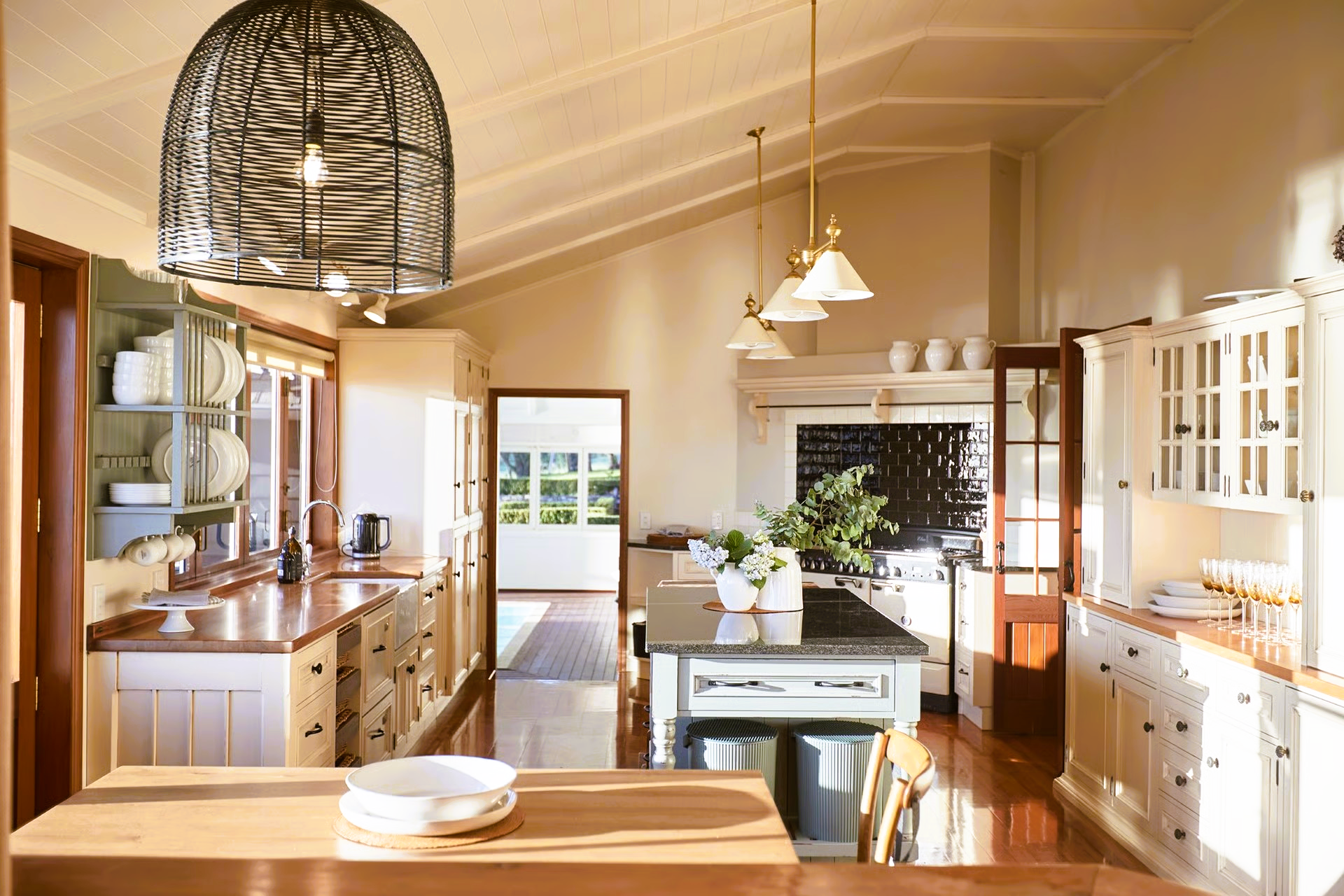 Spacious kitchen with white cabinets, wooden counters, and a black island, under high ceilings, with natural light.