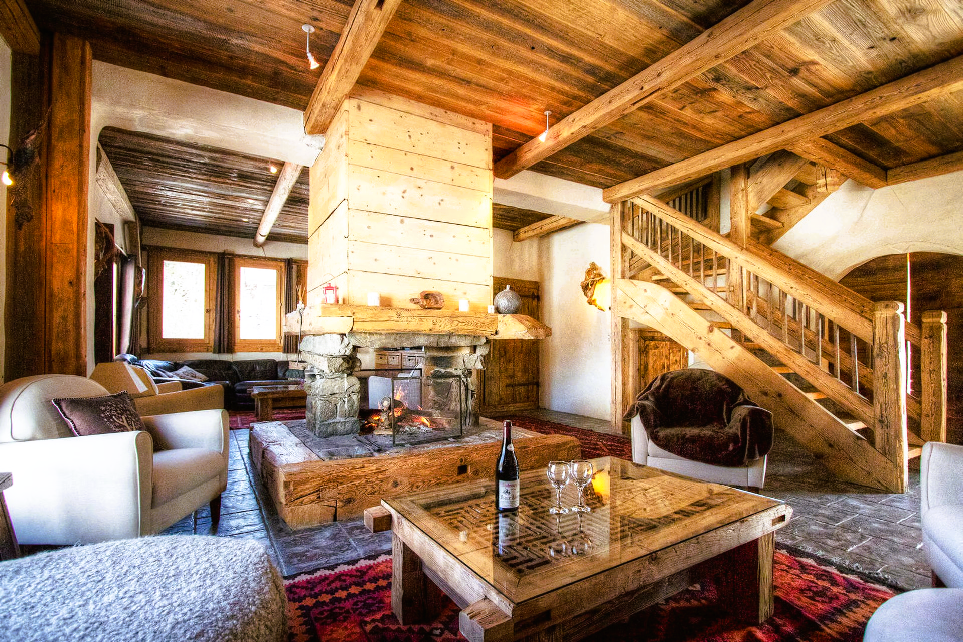 Cozy, rustic living room with fireplace, wood beams, staircase, and seating.