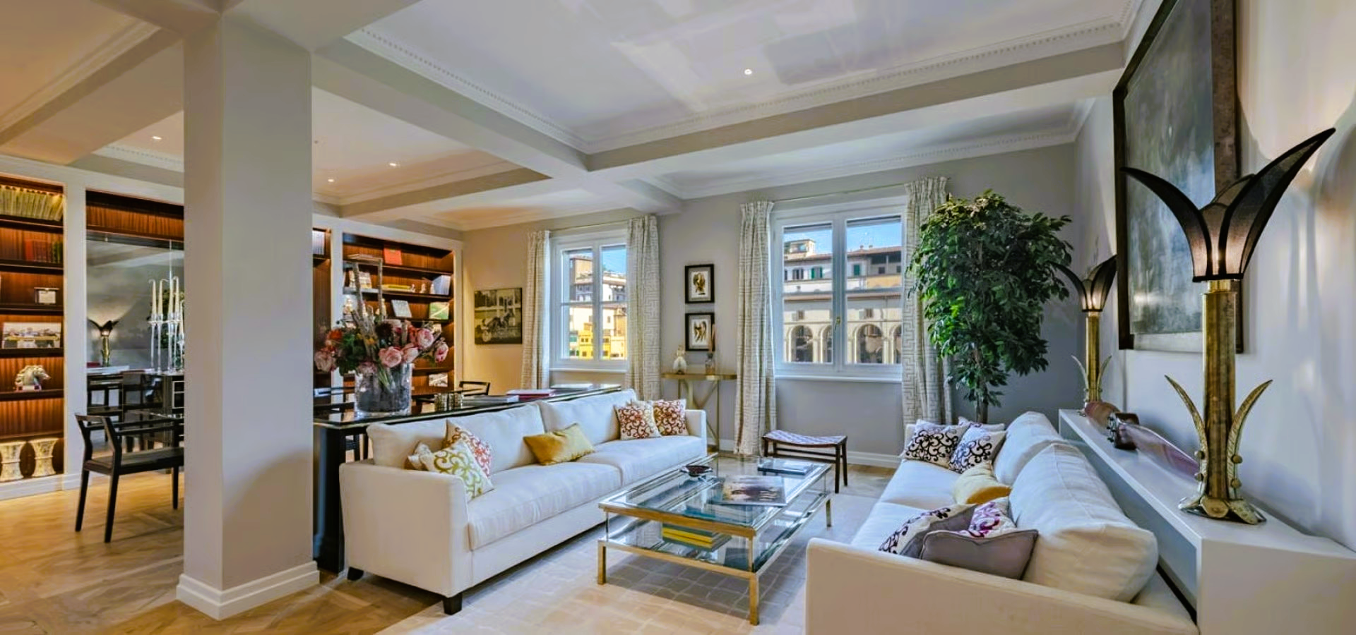Elegant living room with white sofas, glass coffee table, and built-in bookshelves; bright space.