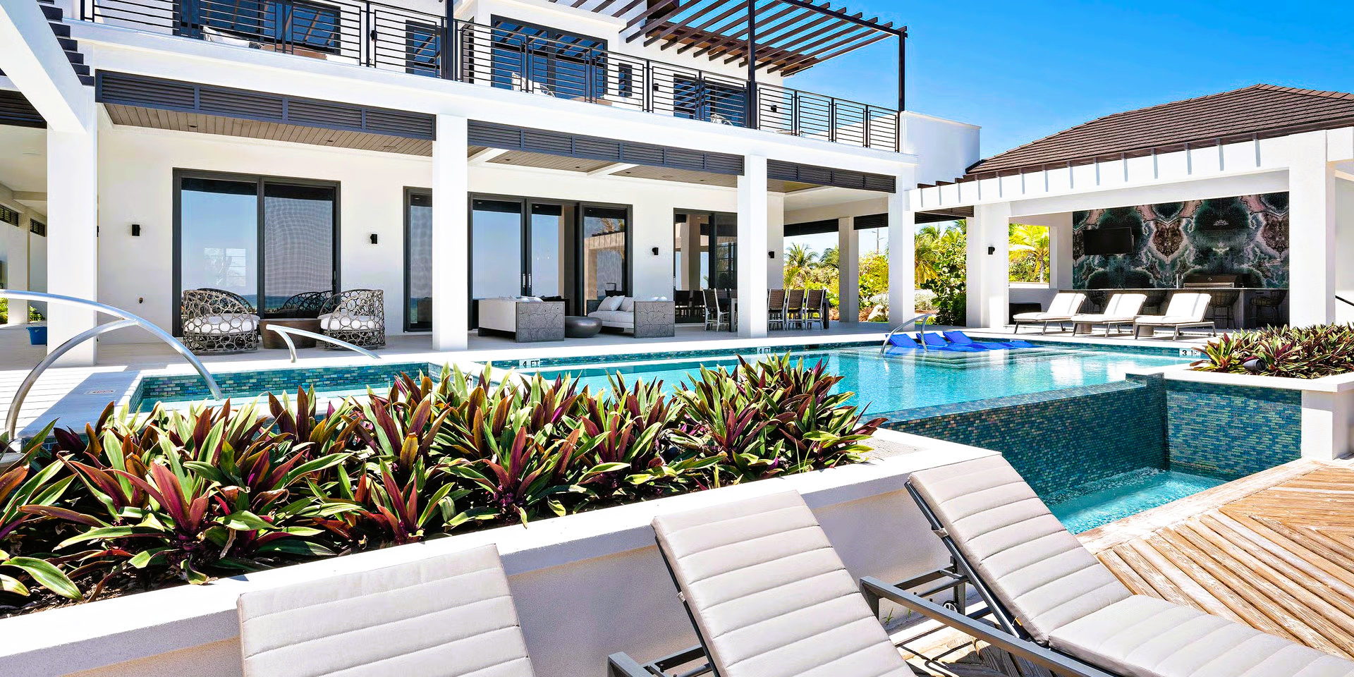Luxury home with pool, deck, and lounge chairs.