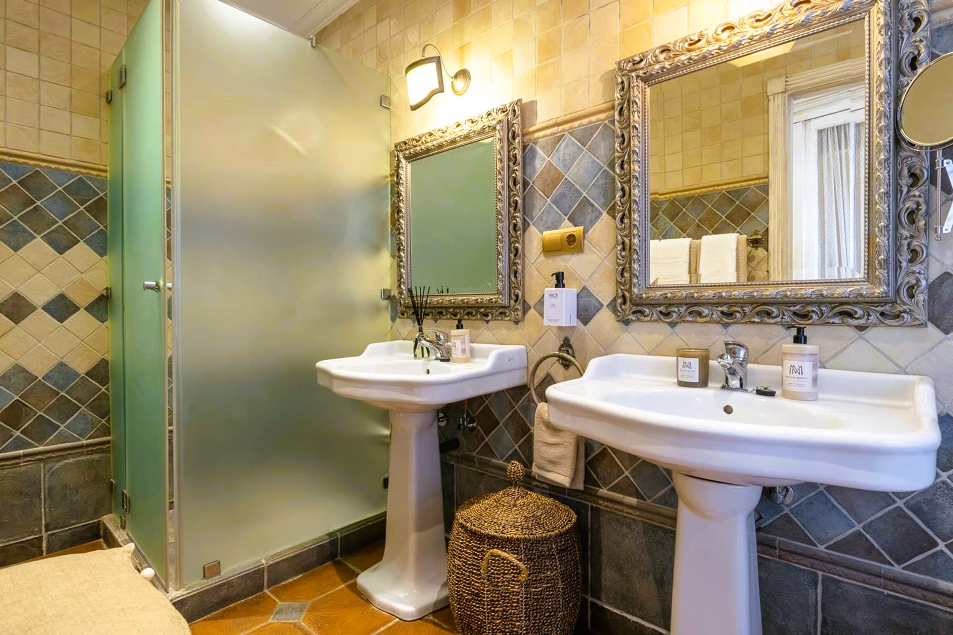 Bathroom with two pedestal sinks, a frosted glass shower, and ornate mirrors.