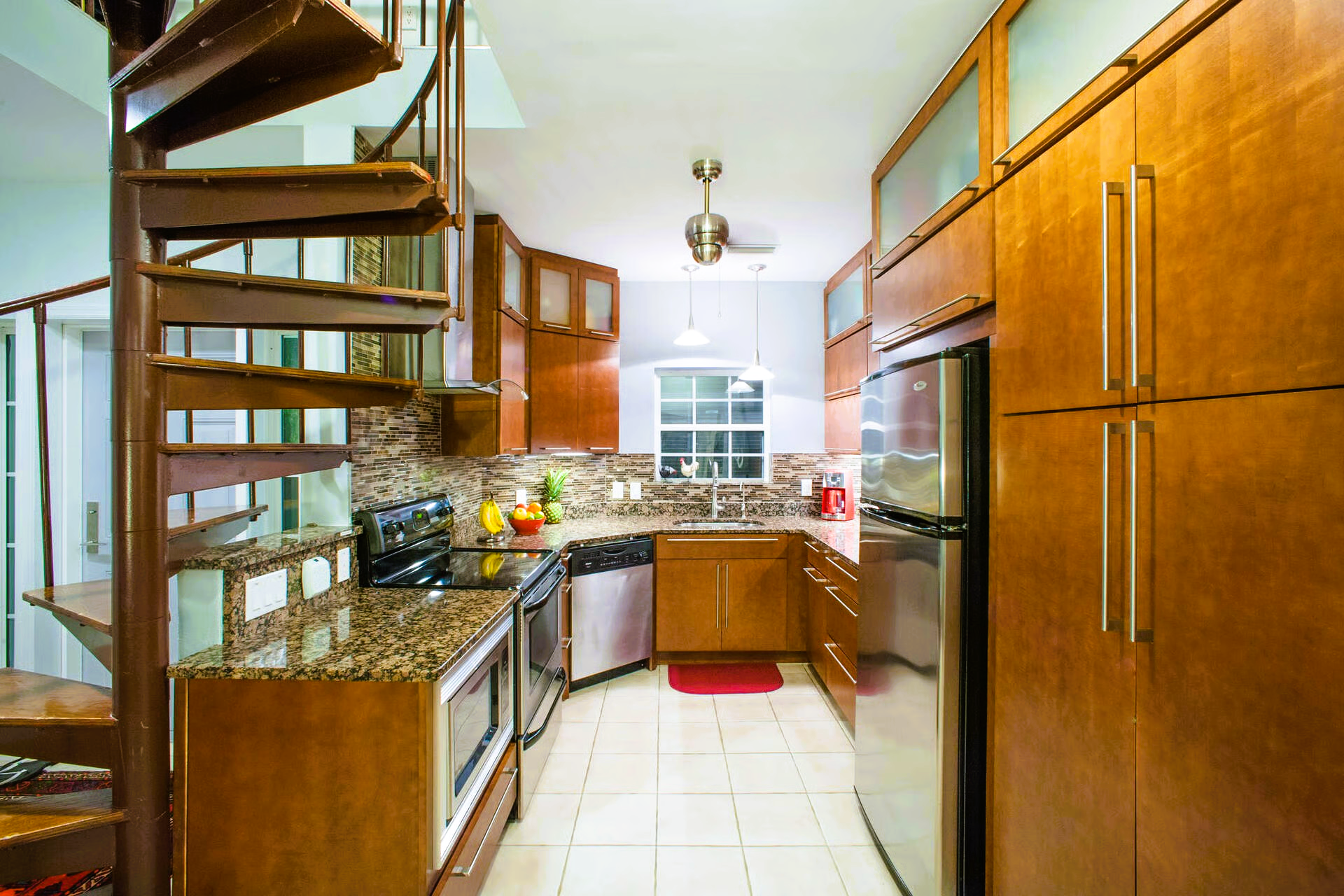 Kitchen with spiral staircase, brown cabinets, stainless steel appliances, and beige tile floor.