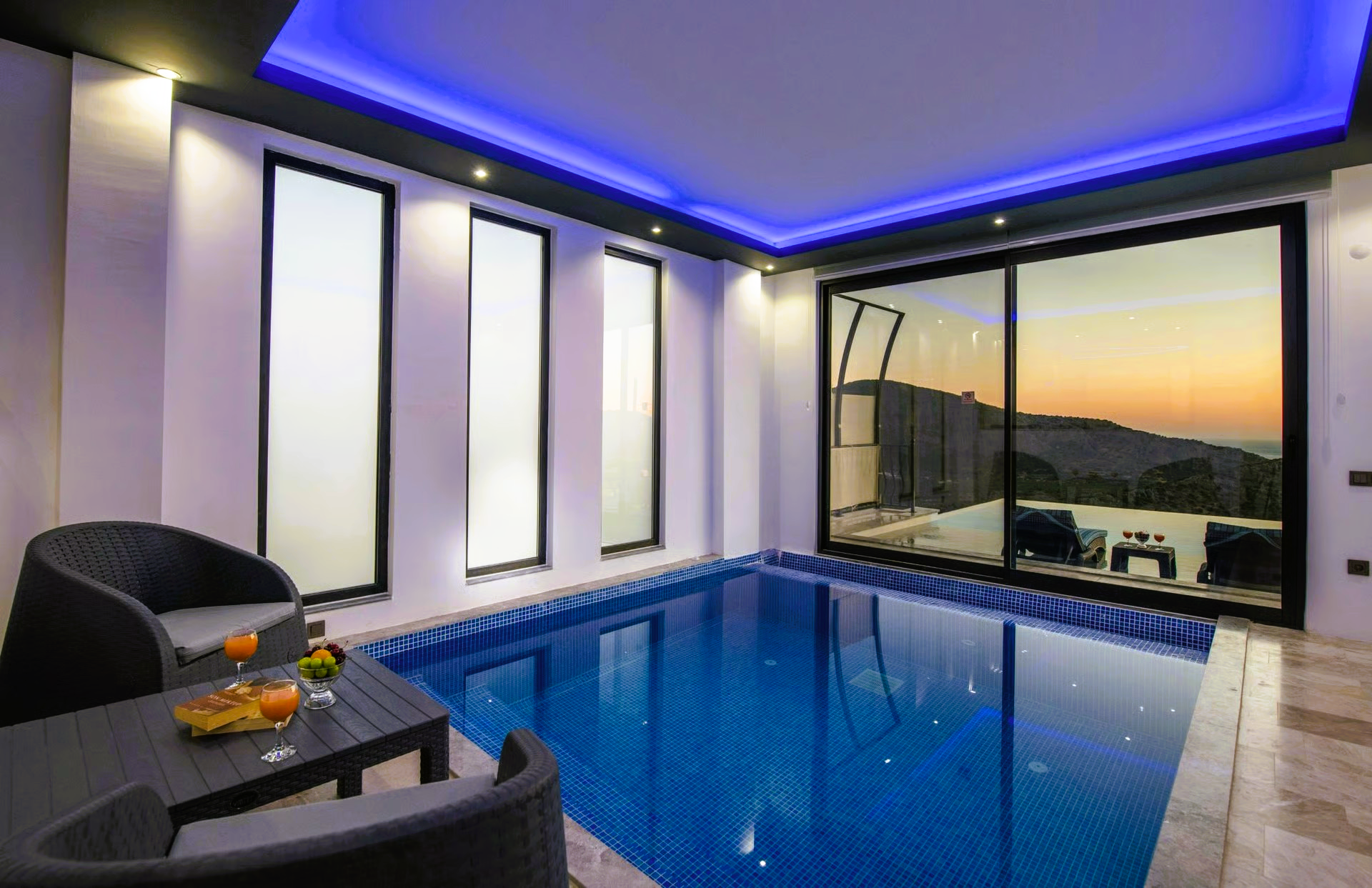 Indoor pool with blue tile, two armchairs, sliding glass door, and view.