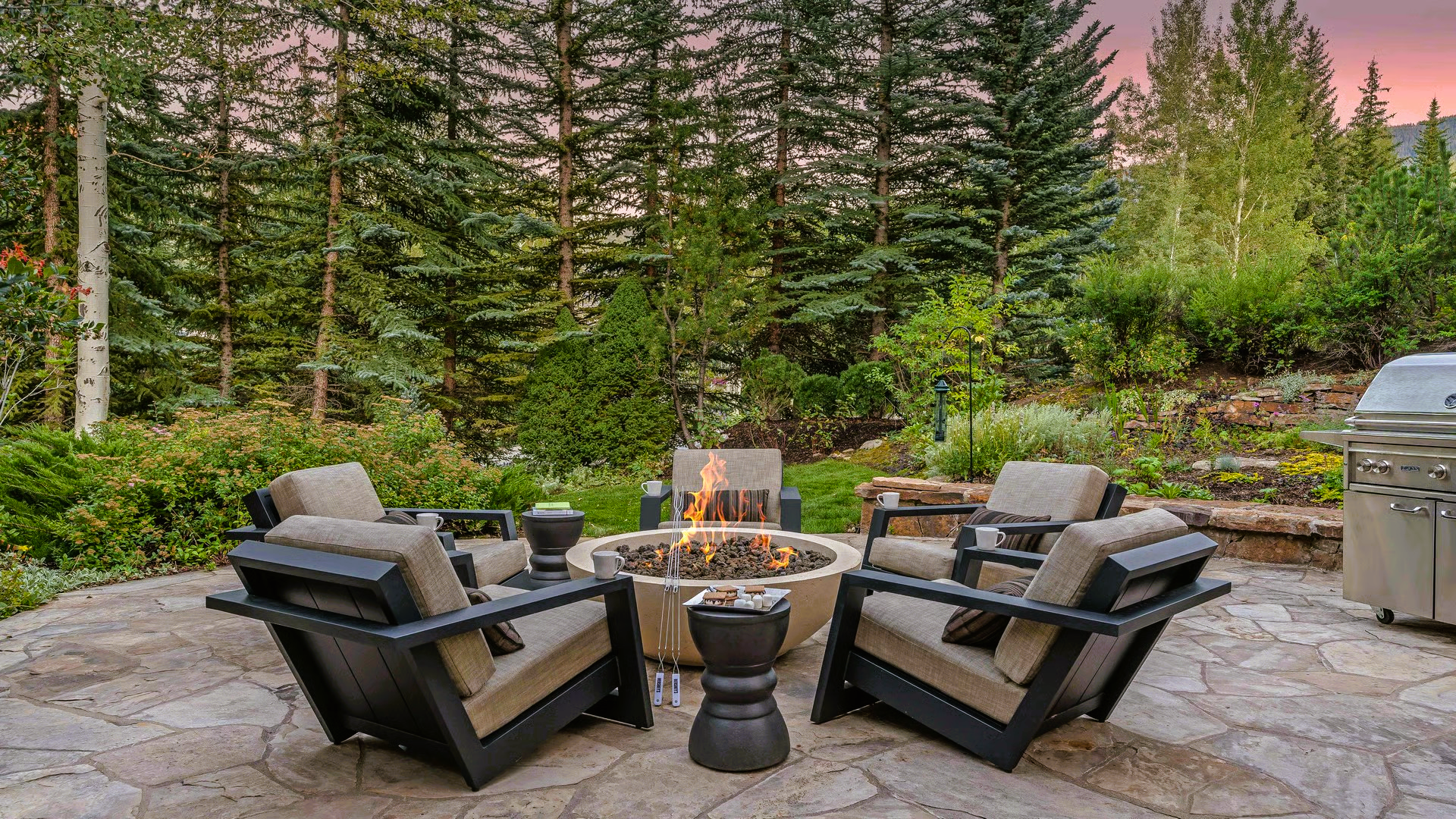 Patio with fire pit, surrounded by armchairs, with trees in the background.