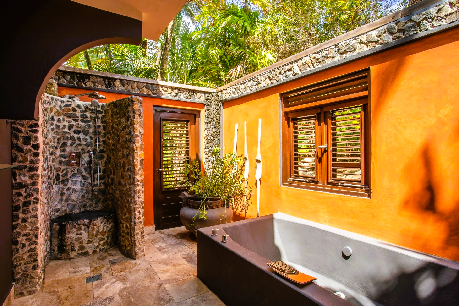 Outdoor bathroom with a stone shower, orange walls, and a gray bathtub.