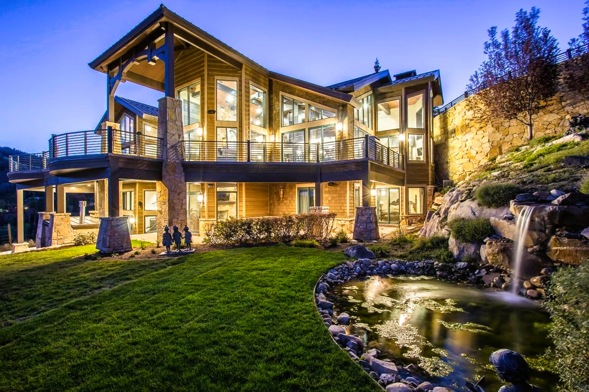 Luxury home with a pond and waterfall, lit up at dusk.