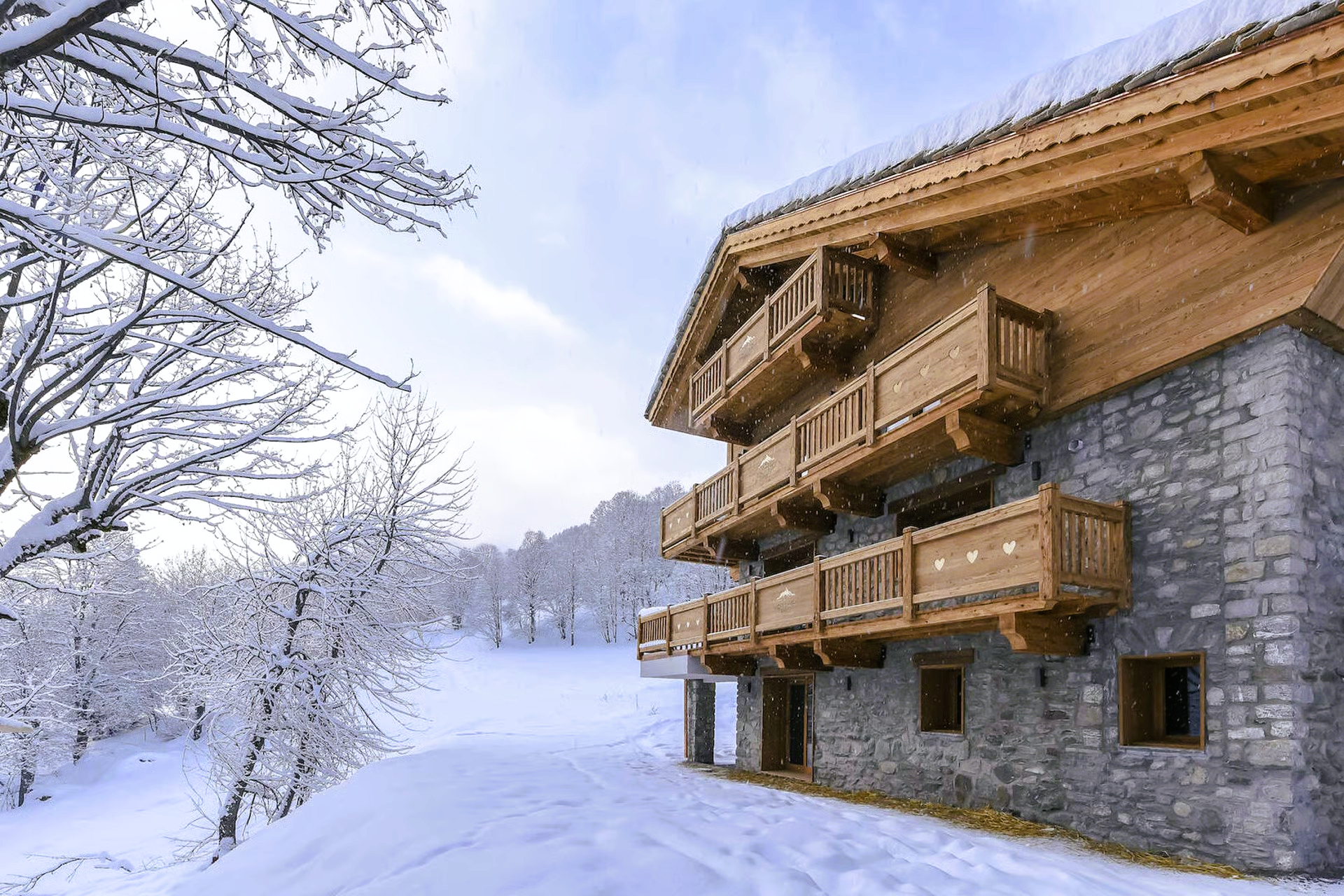 Snow-covered wooden chalet with balconies, surrounded by snow-covered trees on a sunny winter day.
