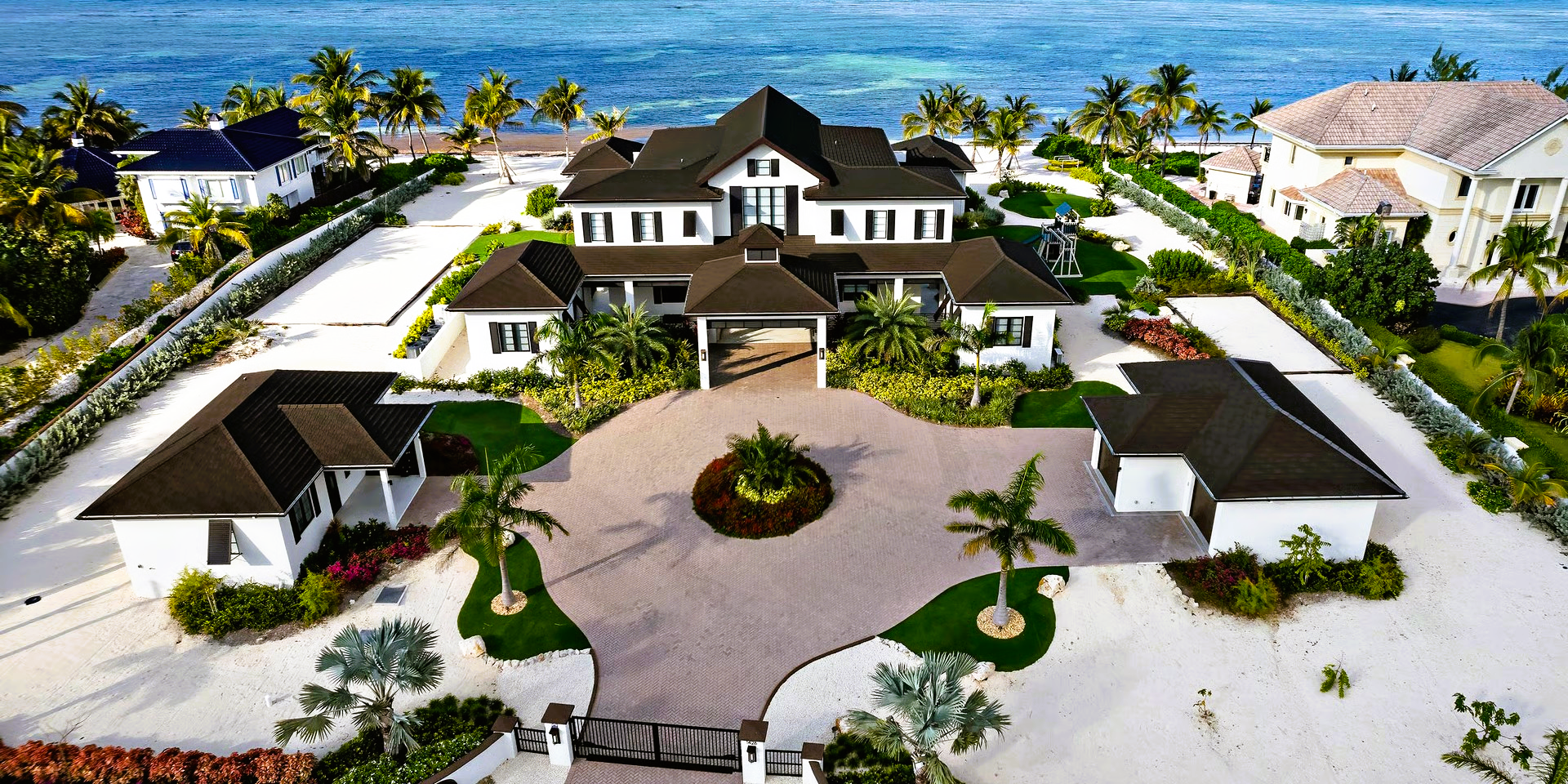Luxurious beachfront mansion with a large circular driveway and green landscaping.