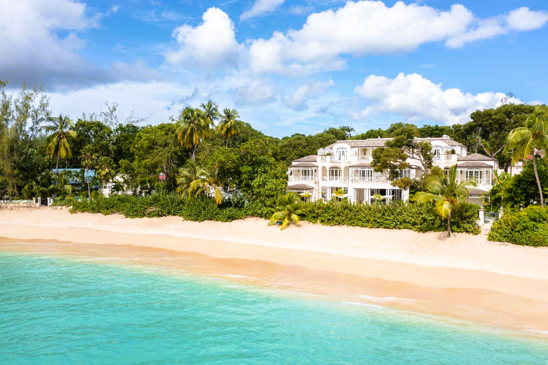 Beachfront mansion with white exterior, turquoise water, and sandy beach.
