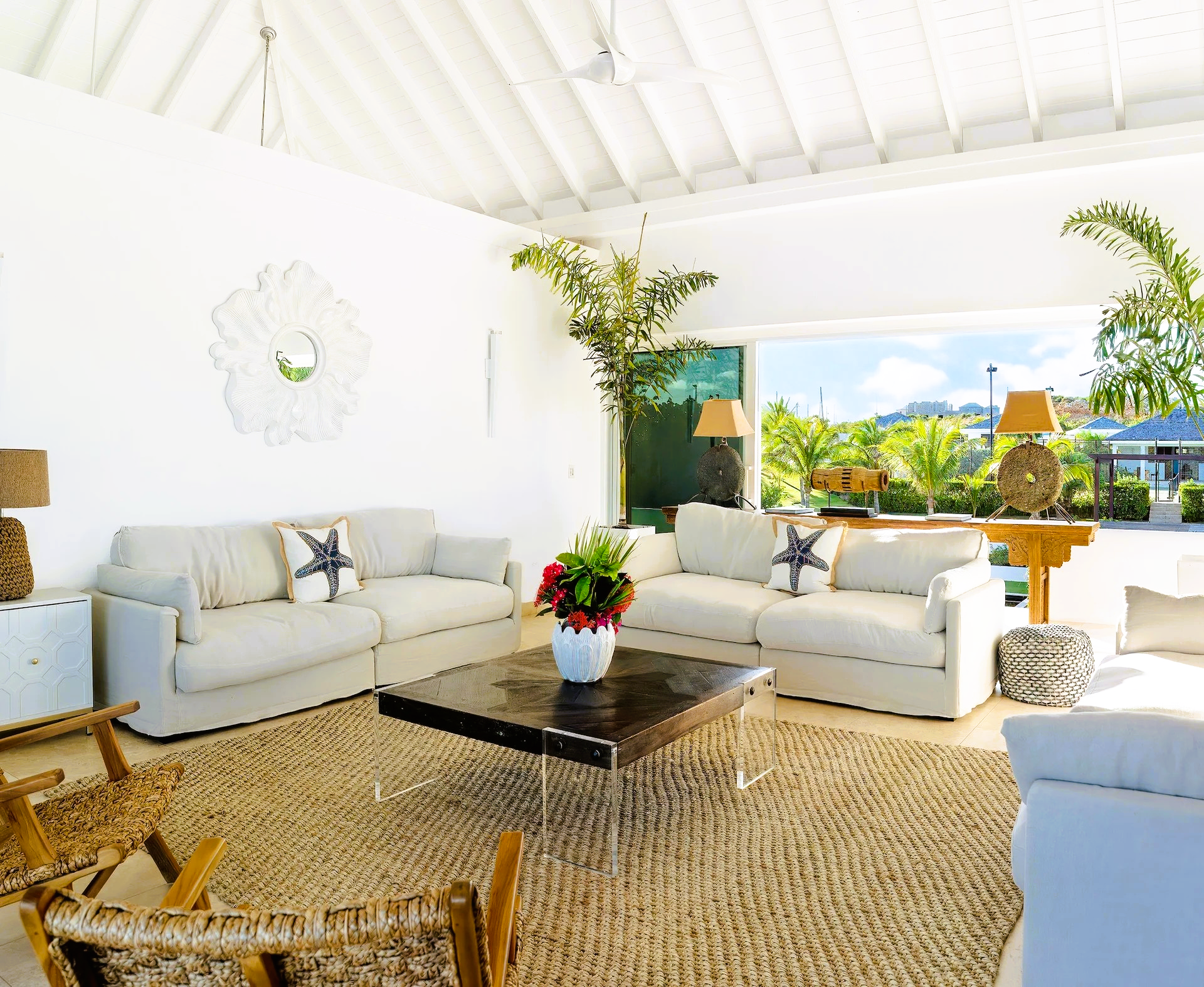 Bright white living room with neutral sofas, natural rug, and large window overlooking greenery.