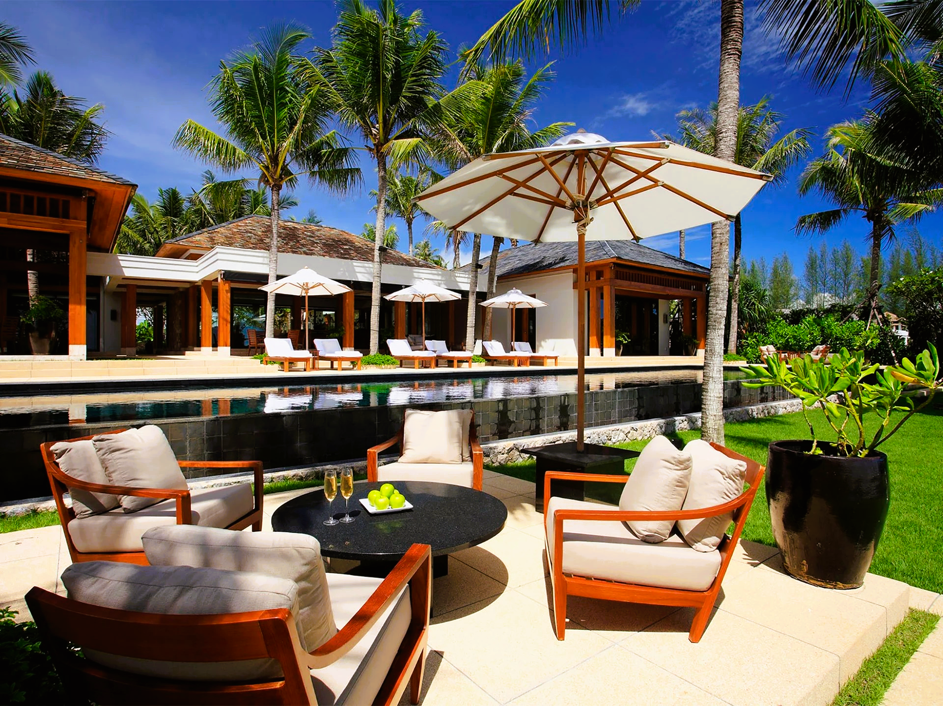 Outdoor seating area with chairs, umbrella, and table, overlooking a pool and villa.