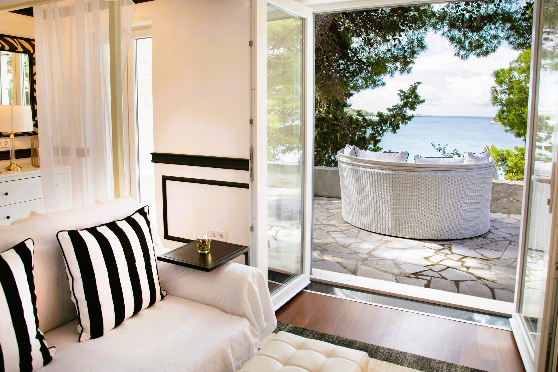 White room with black and white accents opens to a terrace with a hot tub overlooking the ocean.