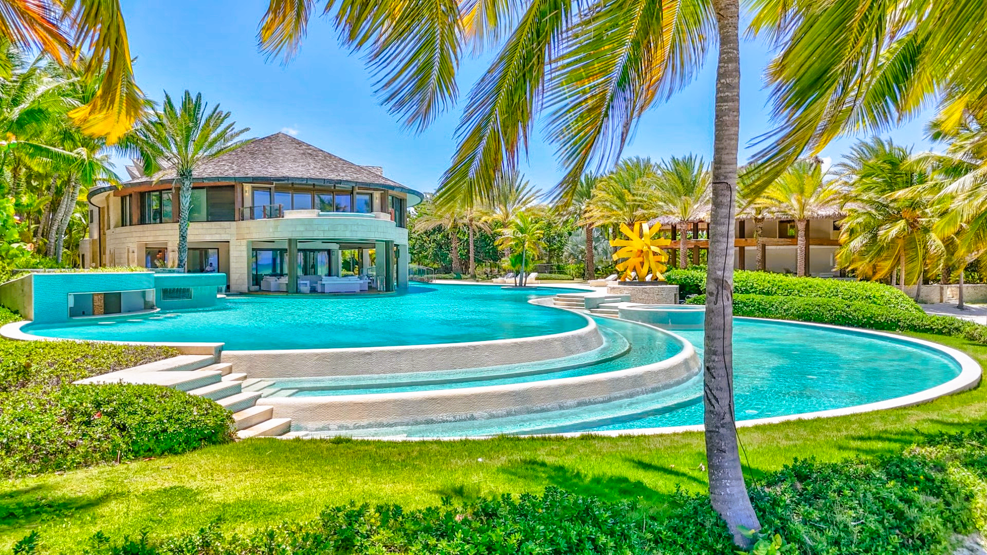 Luxurious villa with a turquoise pool, palm trees, and lush green lawn.