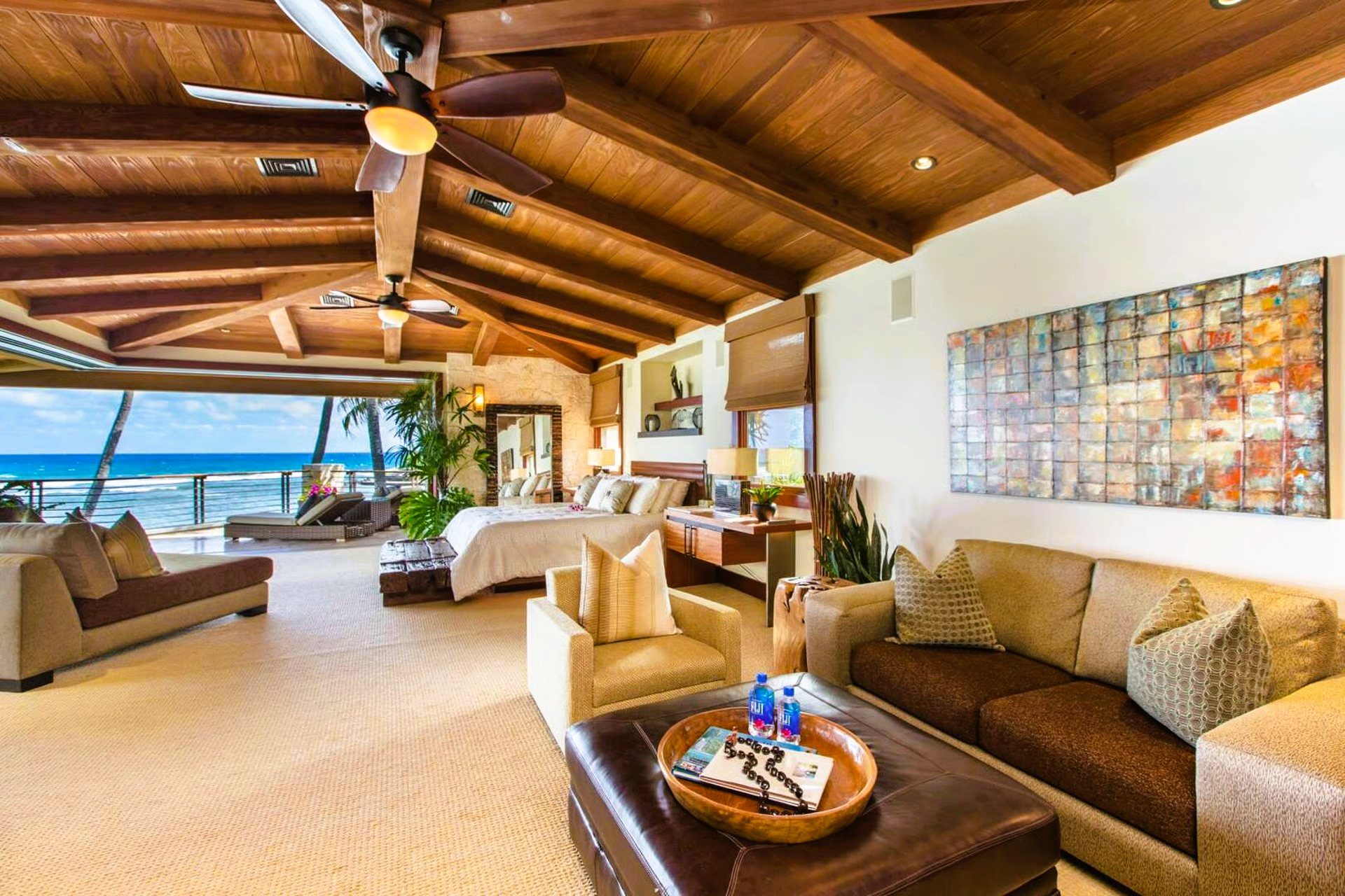 Spacious, ocean-view bedroom with wood beam ceiling, seating area, and open doors to the beach.