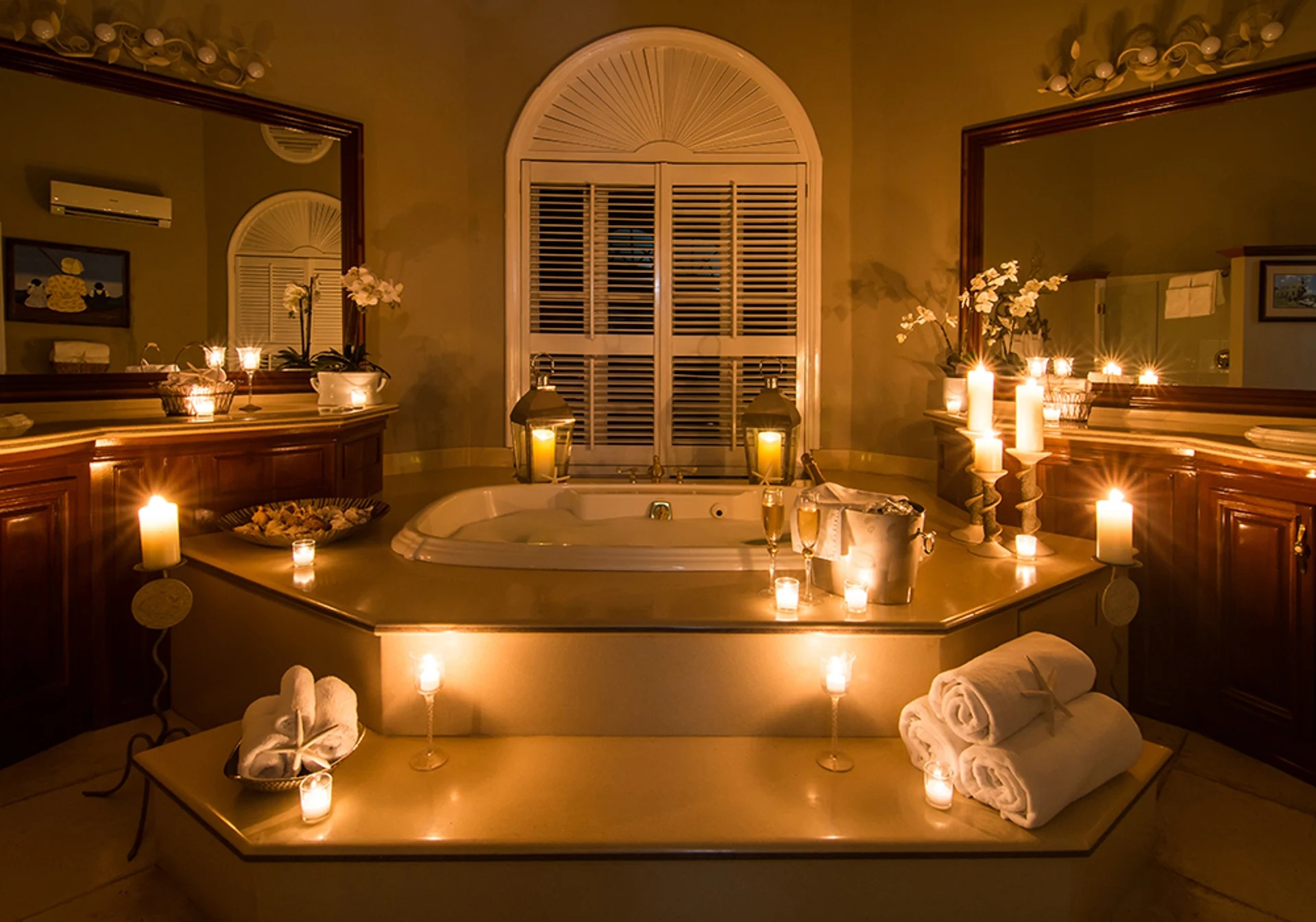 A romantic bathroom with candles lit around a bathtub, towels, and champagne.