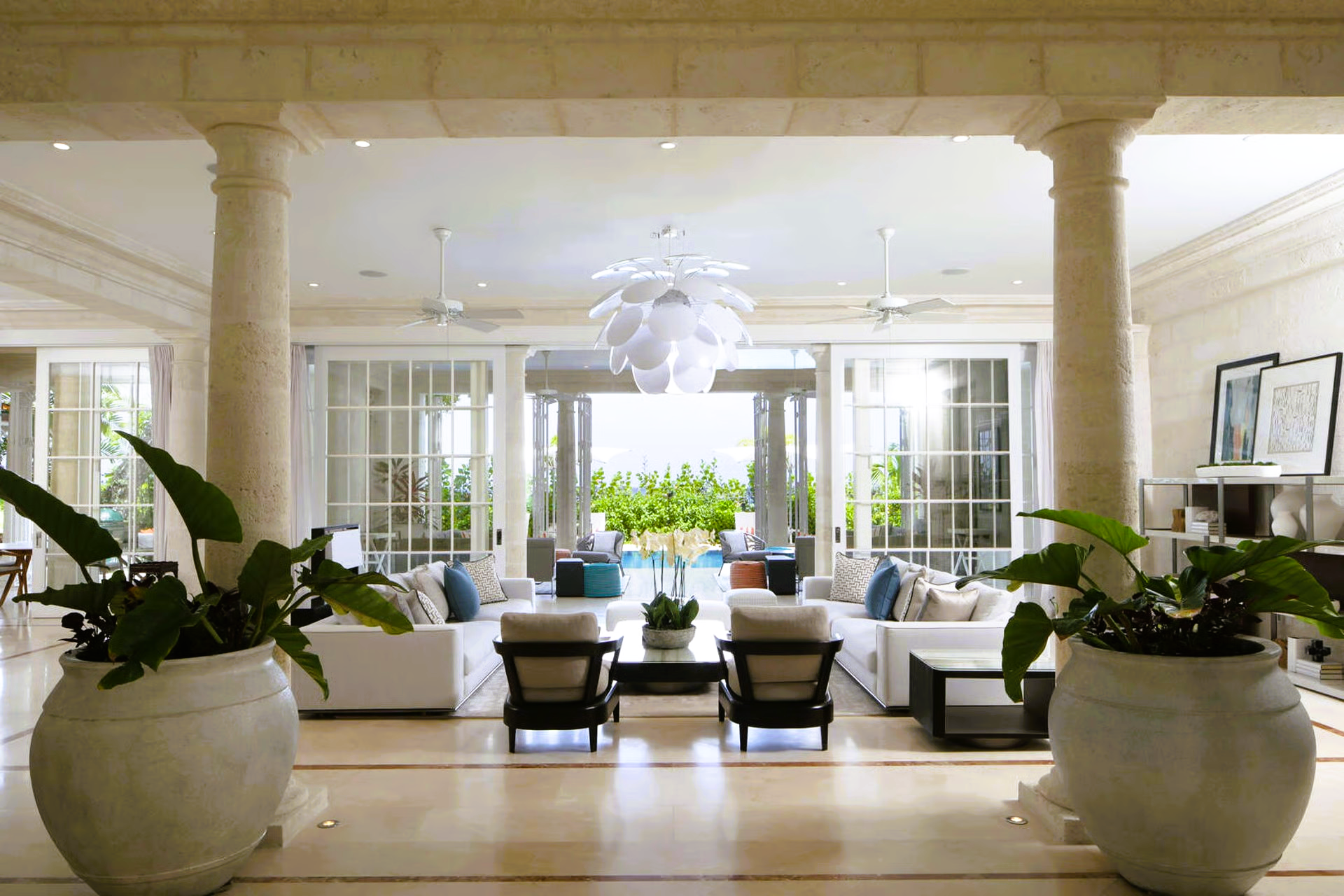 Luxurious light-filled living room with columns, white furniture, and open doors to a pool area.