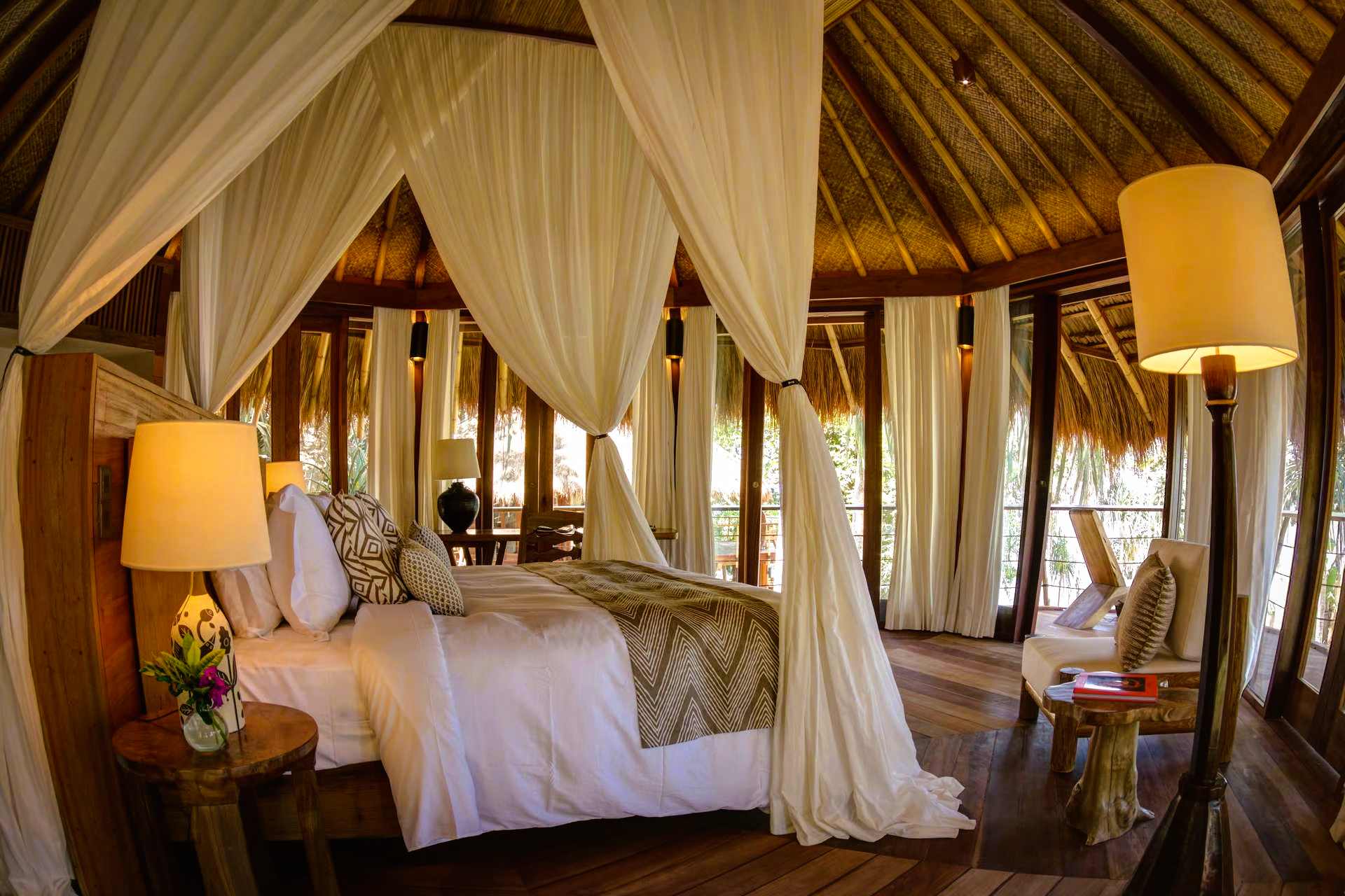 Bedroom with canopy bed, white linens, wooden furniture, and floor-to-ceiling windows.
