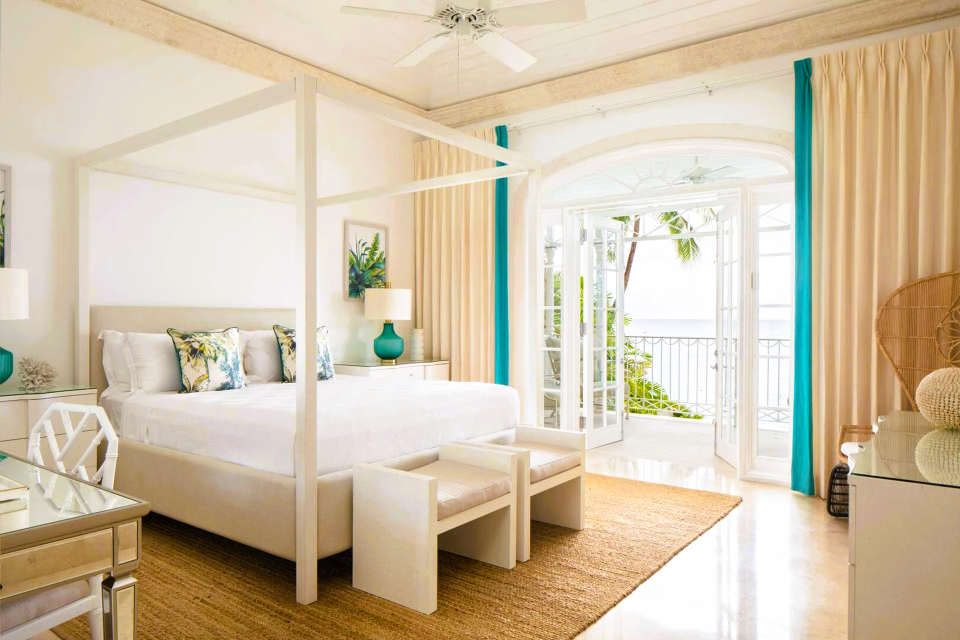 Bright bedroom with a four-poster bed, turquoise accents, and a balcony overlooking the ocean.