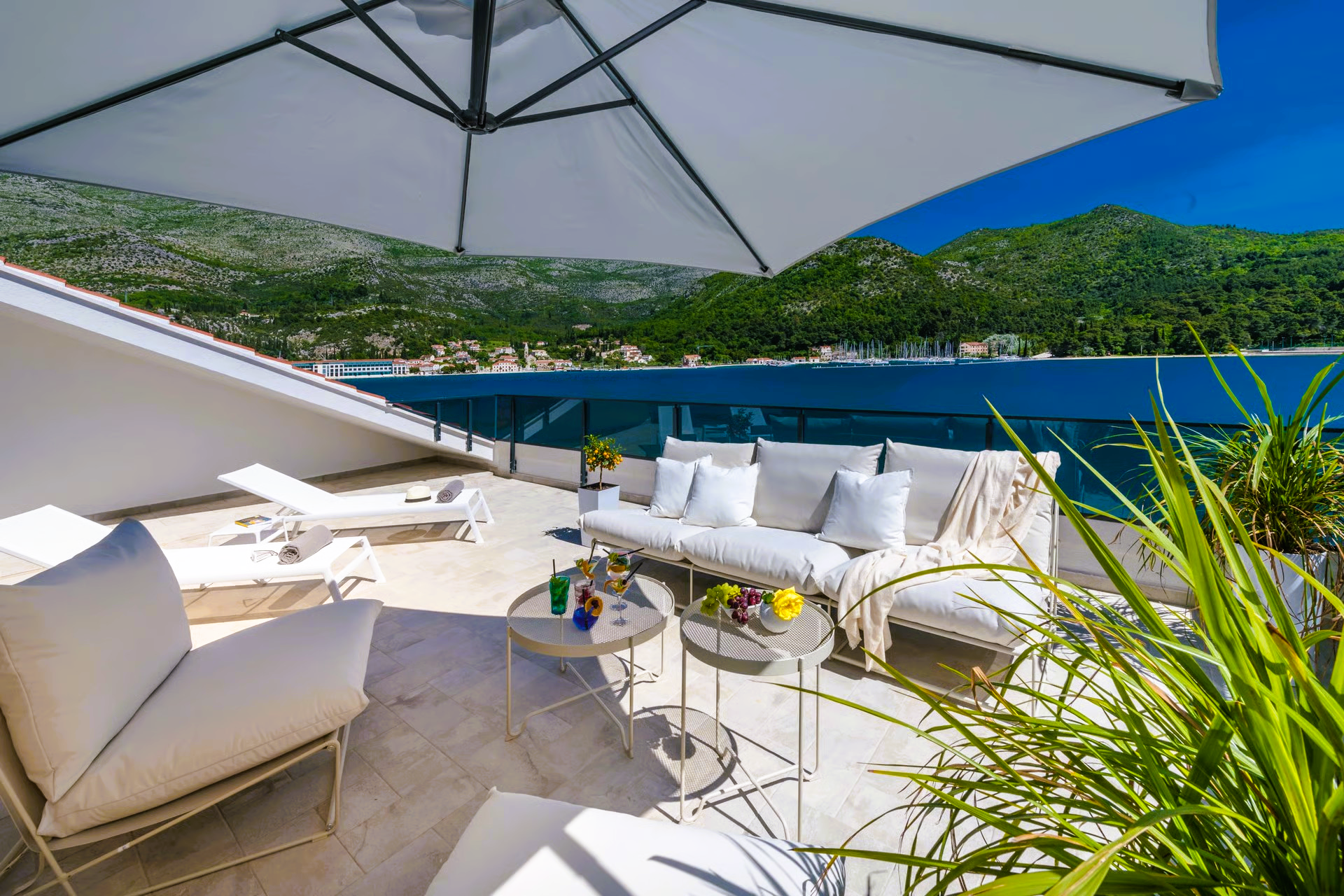 Rooftop patio with white furniture, umbrella, ocean view, and mountains in the background.