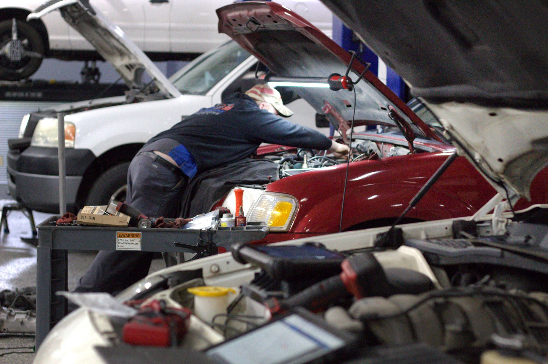 A man is working on a car in a garage with the hood open | Full Throttle Automotive Llc