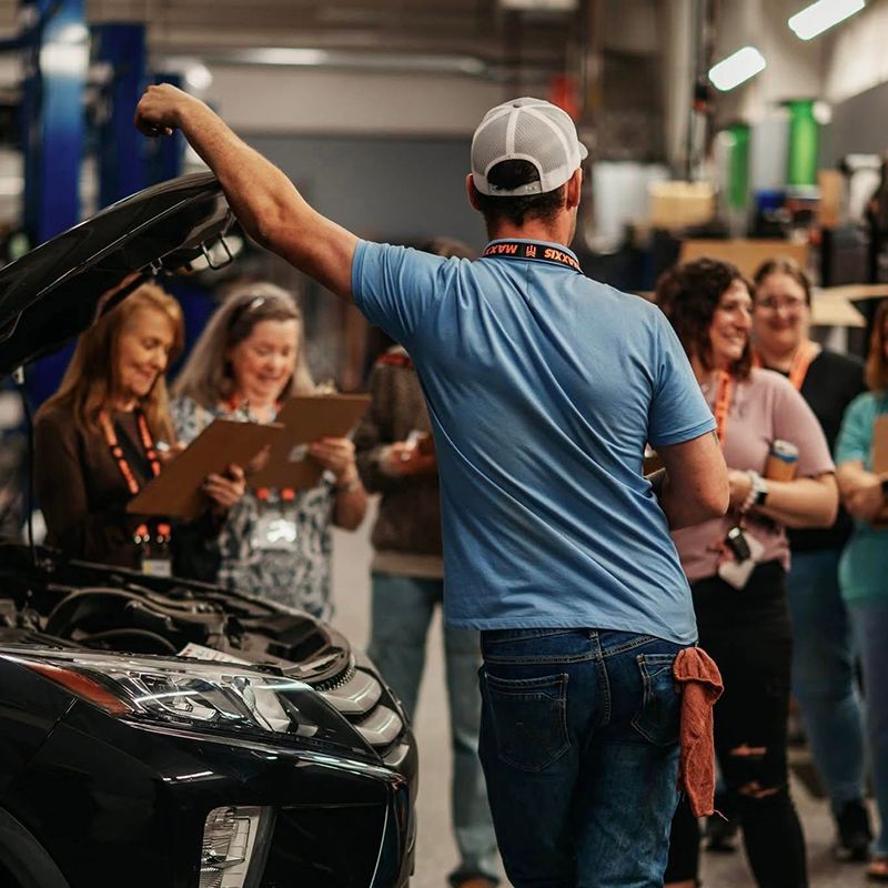 Technician explaining about the under a hood of a car as women take notes during Ladies Night | Full Throttle Automotive LLC
