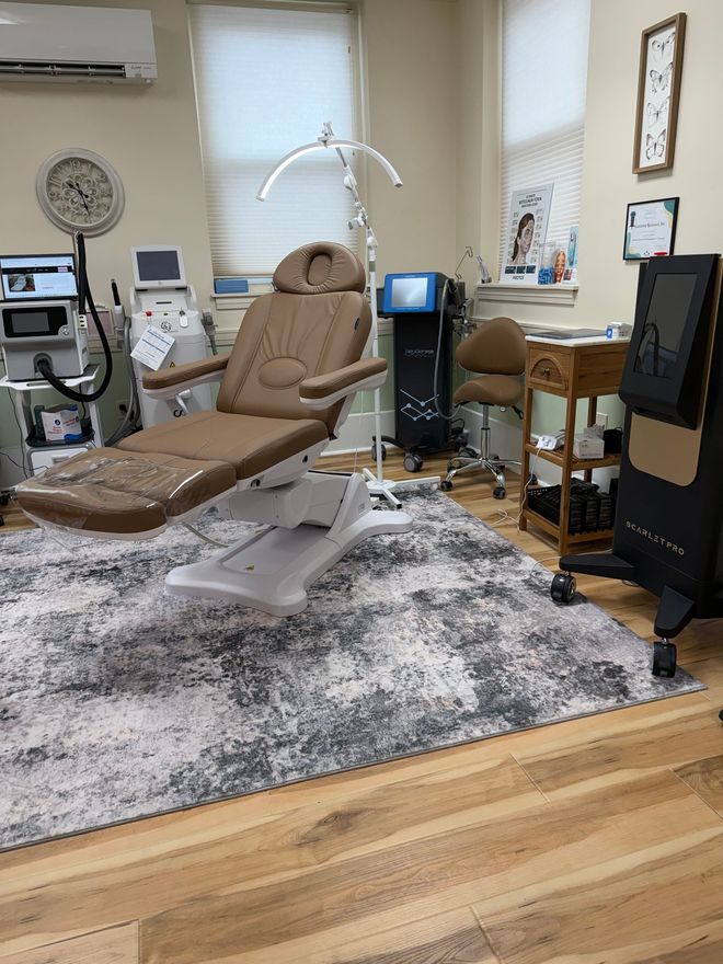 Treatment room with chair, overhead light, and equipment on a gray rug and wood floor.