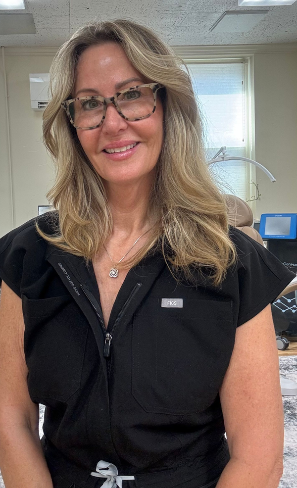 Smiling woman in black zip-up jacket standing in an office, wearing glasses.