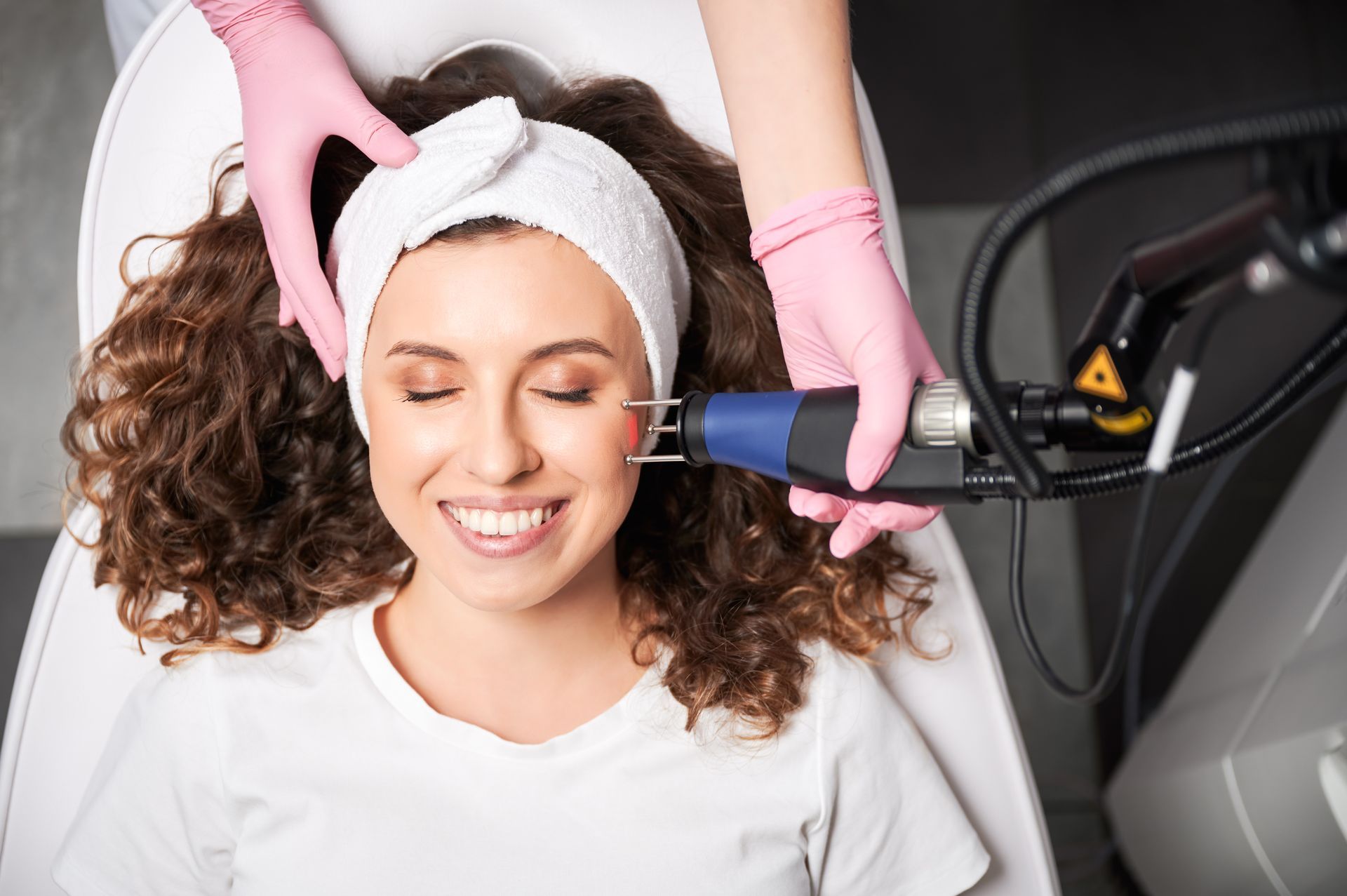 Woman getting a facial treatment with a handheld device while smiling in a spa setting