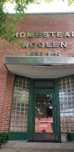 A brick building with a green door and a sign that says homestead woolen mills.
