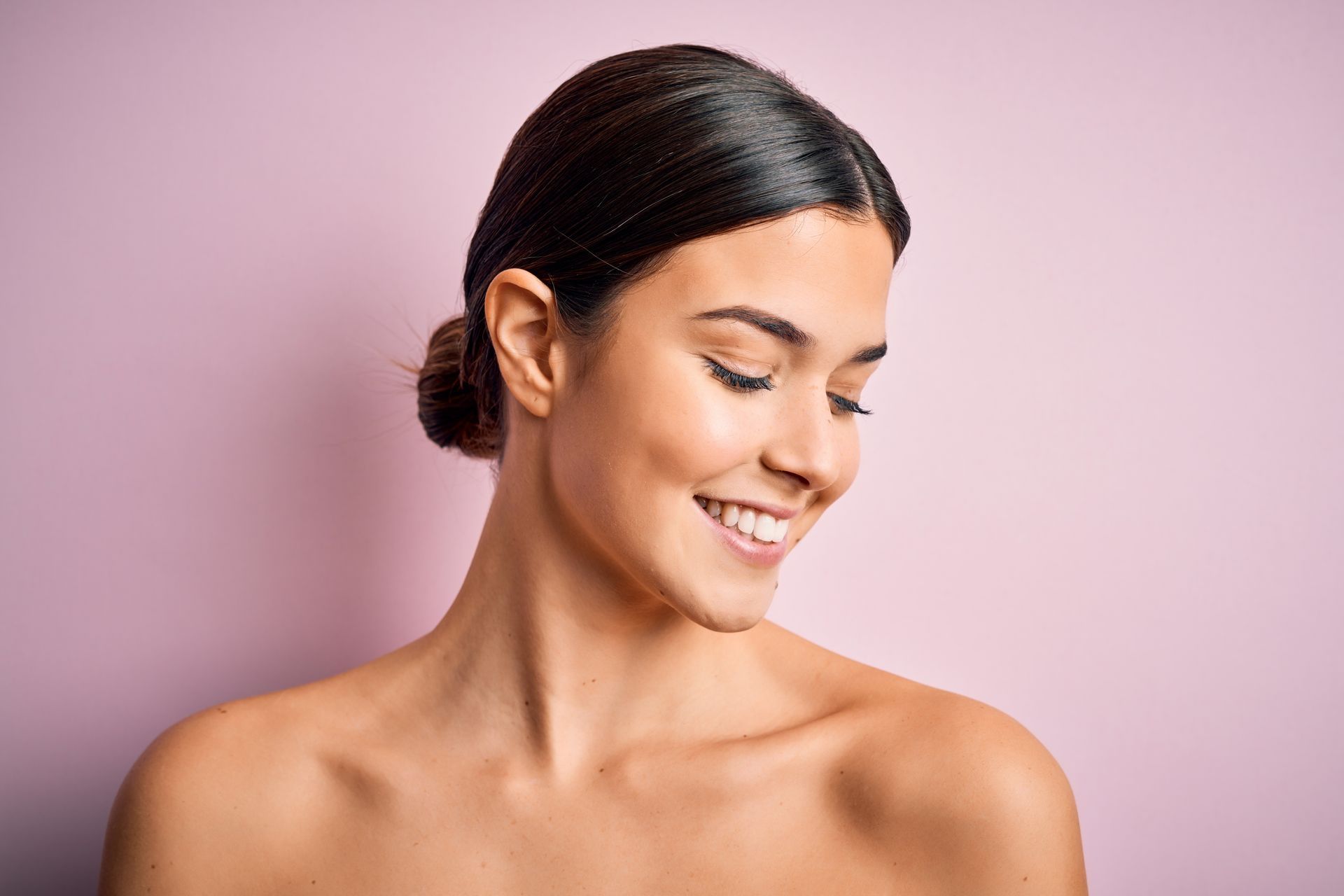 A woman is smiling with her eyes closed and her hair in a bun.