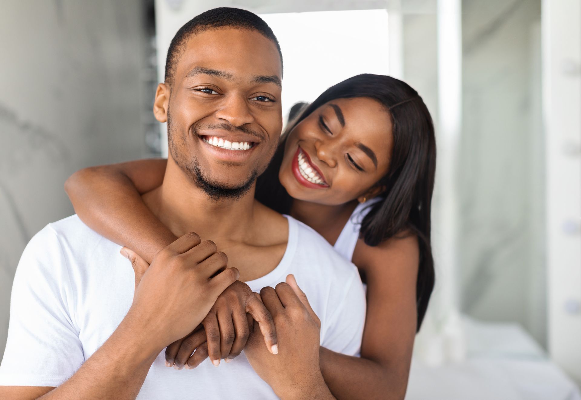 A woman is hugging a man from behind and smiling.