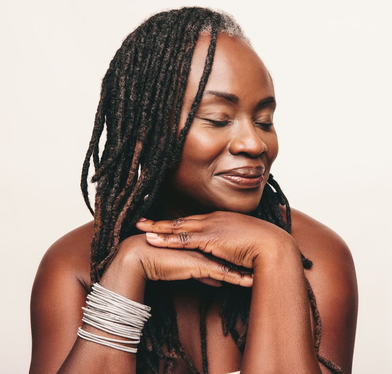 A woman with dreadlocks is smiling with her eyes closed and her hands on her face.