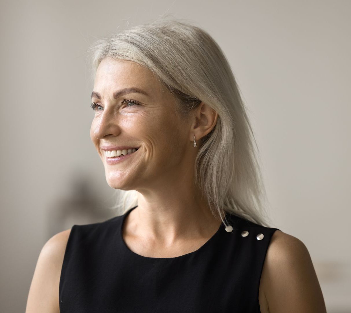 A woman with gray hair is smiling and wearing a black dress.