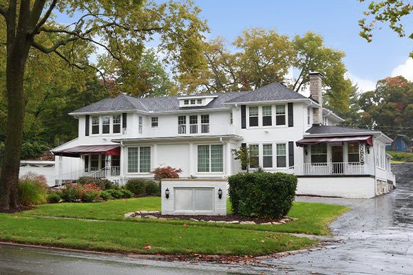 White two-story building with dark shutters and awnings. Green lawn and trees in front.