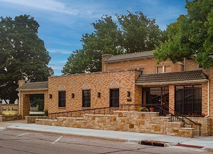 Brick building with wheelchair ramp and stone facade. Trees frame the sky above the structure.