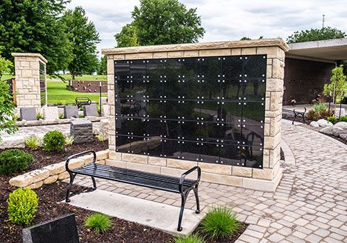 Black granite columbarium with a bench in a cemetery setting.