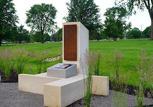Monument with a rusted metal panel, on a grassy field with trees in the background.