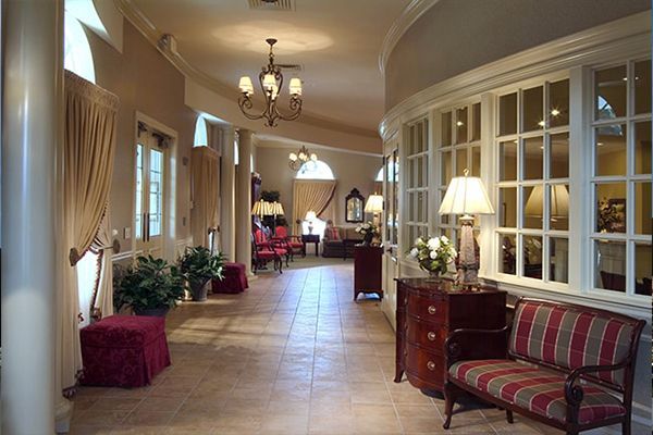 Elegant, curved hallway with windows, red-striped bench, plants, and a chandelier.