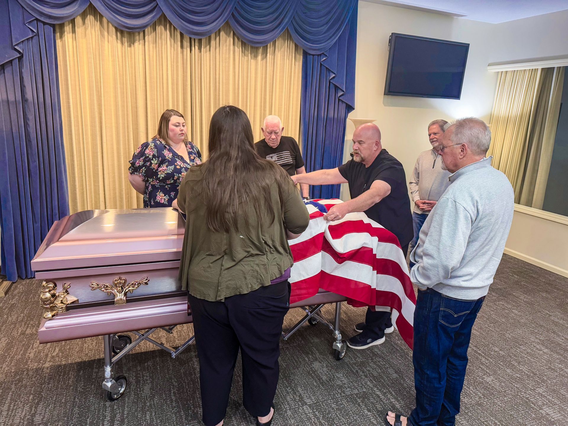 Interior of a funeral home chapel with chairs, casket, podium, and screen.