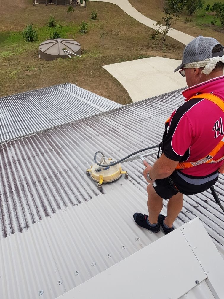 A Man in a Red Shirt is Cleaning the Roof of a House — Blast H2O In Proserpine, QLD
