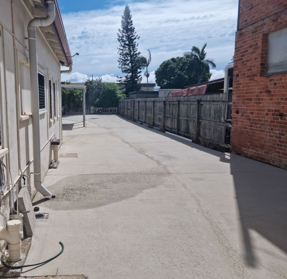 A Woman is Using a Pressure Washer to Clean a Driveway — Blast H2O In Airlie Beach, QLD