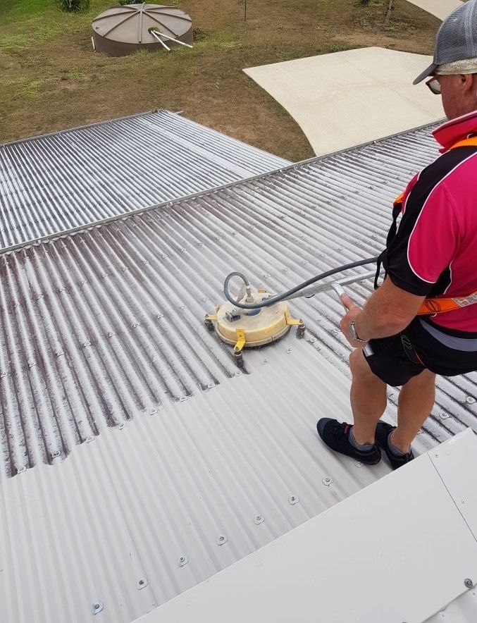 A Man in a Red Shirt is Cleaning the Roof of a House — Blast H2O In Airlie Beach, QLD